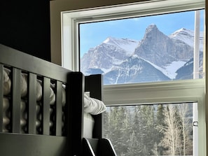 Enjoy breathtaking views of snow-capped mountains from this room's large window, overlooking a forested area below.