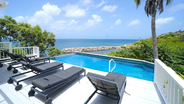 Zona junto a la piscina con sillones, vista despejada del océano y un litoral rocoso.
