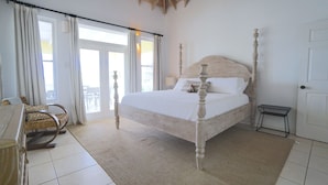 Un dormitorio con cama con dosel, una silla, una mesita y vistas al exterior a través de un ventanal.