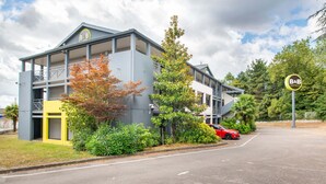 A multi-story hotel with balconies, a parking area, and a red car parked nearby. - B&B Hôtel Nantes Parc Expos La Beaujoire (Nantes)