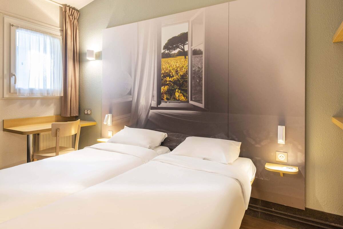 A hotel room with a bed, bedside tables, a window with curtains, and a view of a field.