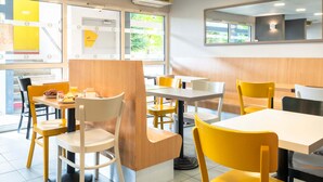 A modern restaurant interior with yellow and white chairs, wooden tables, and large windows allowing natural light. - B&B Hôtel Nantes Parc Expos La Beaujoire (Nantes)