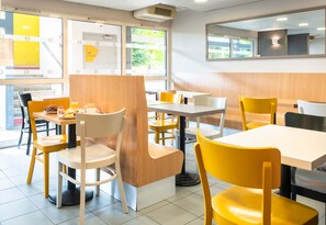 Ein modernes Restaurantambiente mit gelben und weißen Stühlen, Holztischen und großen Fenstern, die viel Tageslicht hereinlassen.