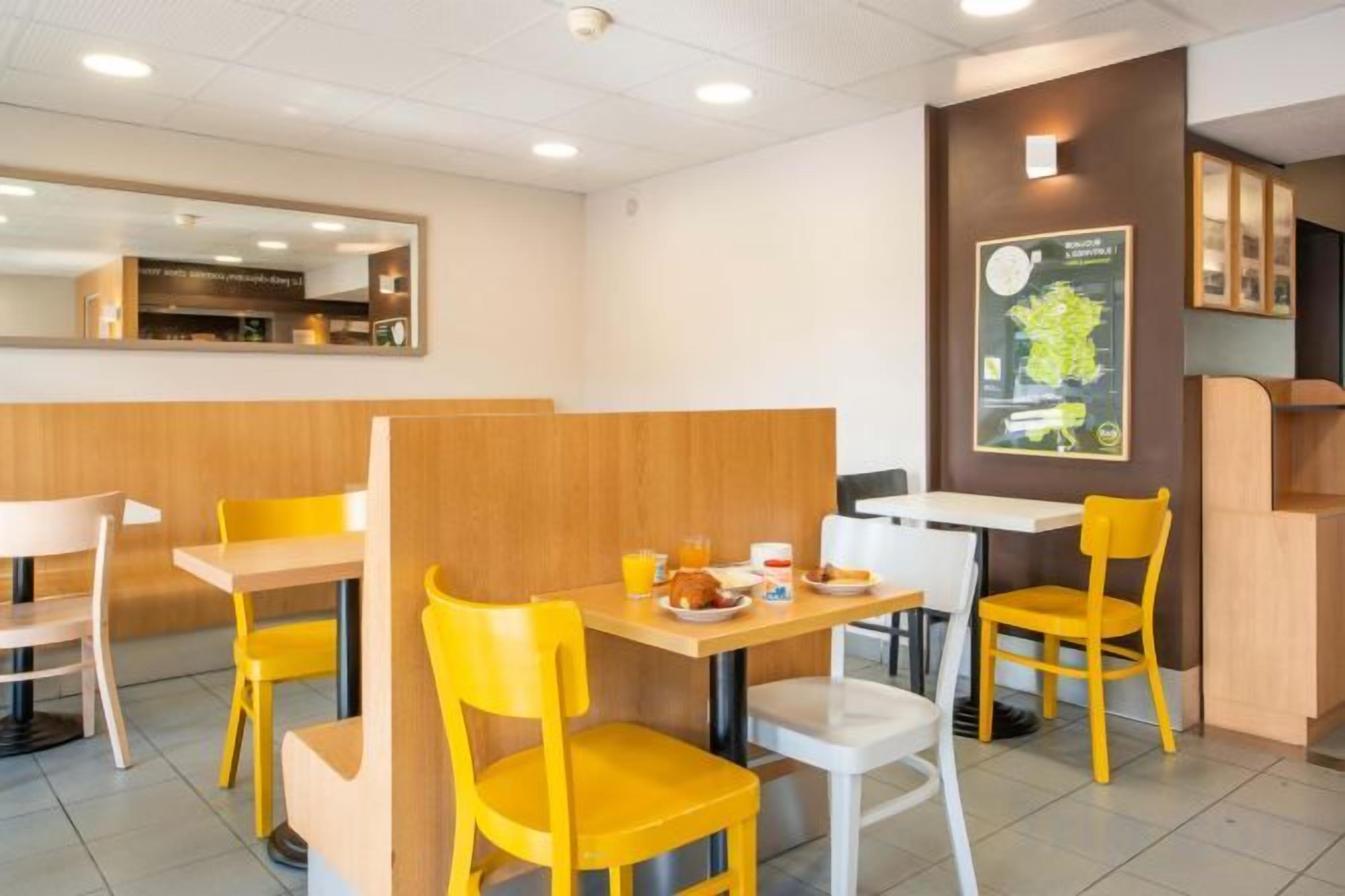 Un interior de restaurante con sillas amarillas, mesas blancas y una partición de madera.