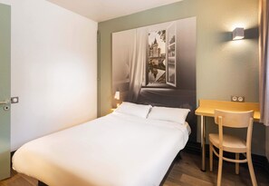A hotel room with a bed, a desk, and a chair. There is a painting on the wall above the bed. - B&B Hôtel Nantes Parc Expos La Beaujoire (Nantes)