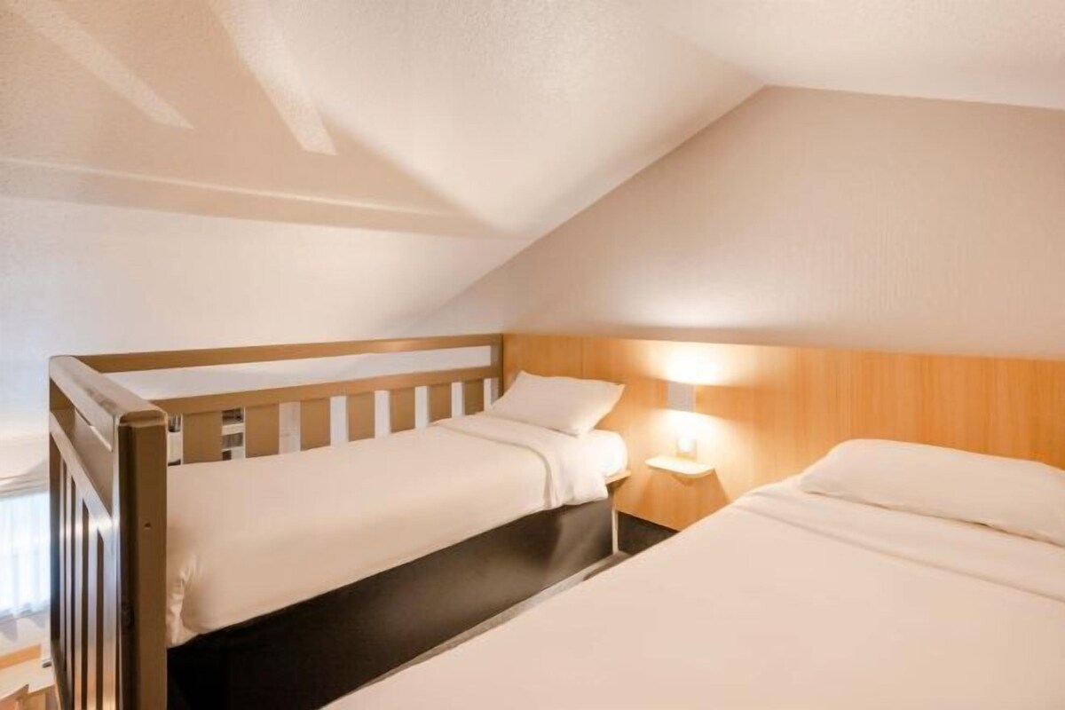 Una camera singola con due letti, una testiera in legno, un comodino con una lampada e un soffitto a falde.