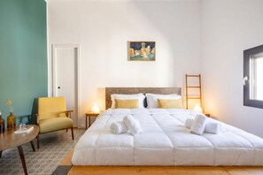 A bedroom with a large bed, a chair, a painting on the wall, and a window.