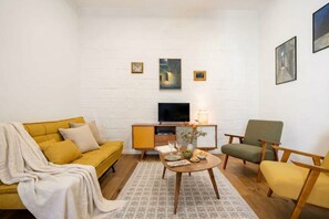 A living room with a sofa, armchair, coffee table, TV, and artwork on the wall.