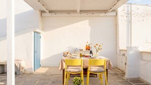A small outdoor dining area with a table set for two, chairs, a coffee table with a book and cups, and a blue door in the background. - Art House with a Terrace in the Historic Center (Monopoli)