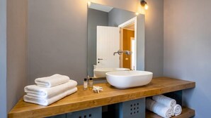 A bathroom with a wooden vanity, a white sink, and a mirror. There are towels stacked on the vanity and a towel rack below. - Art House with a Terrace in the Historic Center (Monopoli)