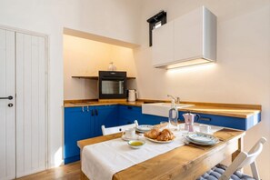 A compact kitchen with a microwave, oven, and sink. A wooden dining table with plates and a bottle of water is set.