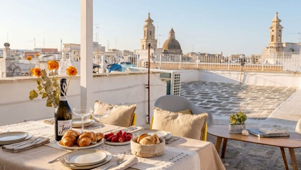 A rooftop terrace with a table set for dining, a bottle of wine, and a view of the cityscape. - Art House with a Terrace in the Historic Center (Monopoli)
