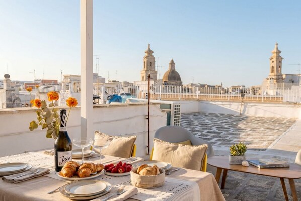 A rooftop terrace with a table set for dining, a bottle of wine, and a view of the cityscape.
