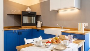 A modern kitchen with blue cabinets, a wooden countertop, a built-in oven, and a dining area with a table set for breakfast. - Art House with a Terrace in the Historic Center (Monopoli)