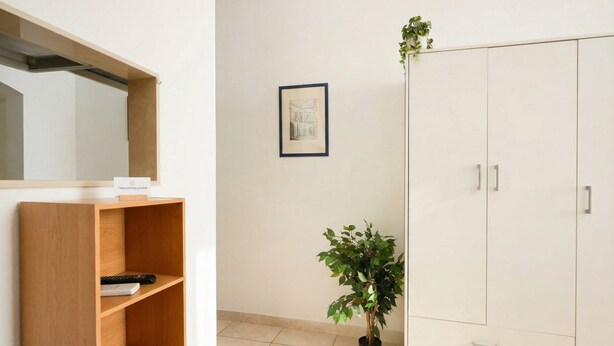 Een kamer met een houten plank, een potplant, een kledingkast en een lijst met een foto aan de muur.