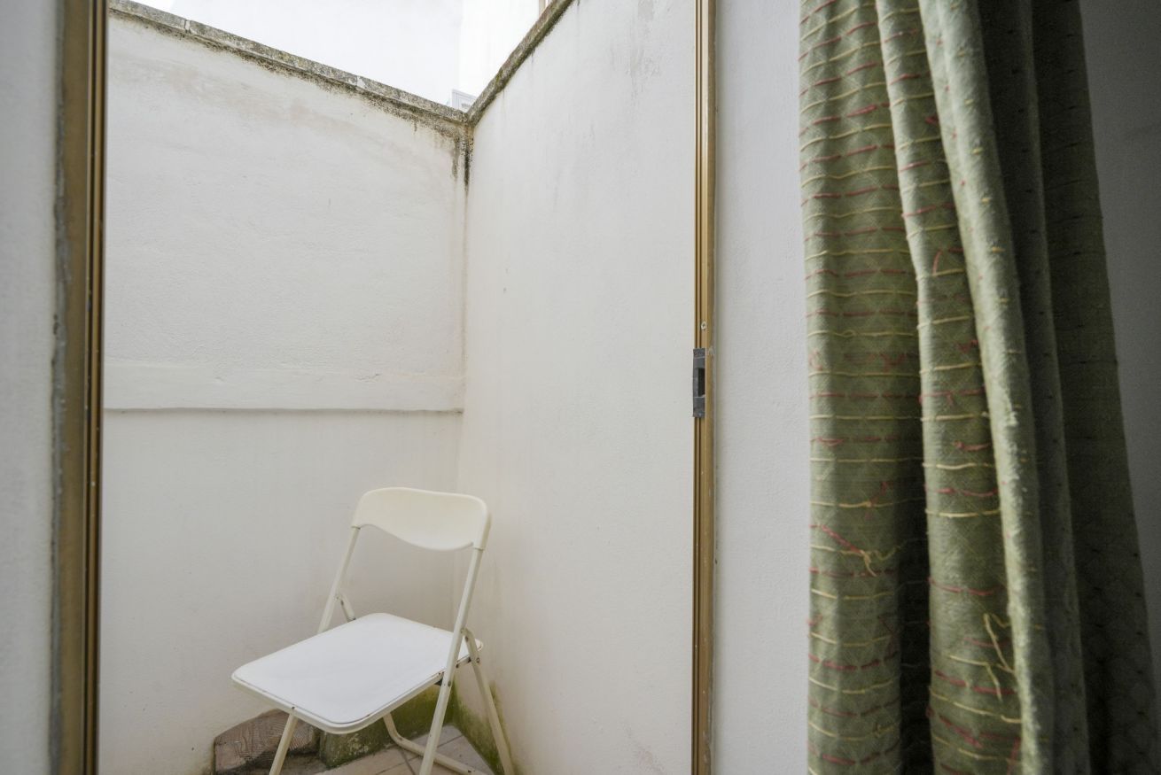 A small, enclosed space with a white chair, a window, and a curtain.