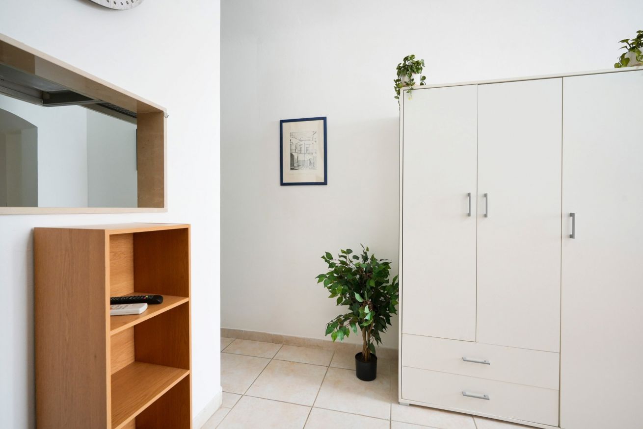Um quarto com estante de madeira, guarda-roupa branco, planta em vaso e um desenho arquitetônico emoldurado na parede.