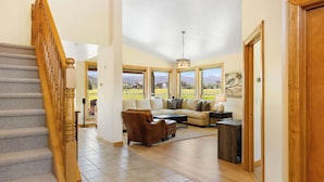 A spacious living area with a wooden staircase, a sofa set, and large windows offering a view of the outdoors. - *New Listing* 4 Bedroom House w/ Private Hot Tub (Big Sky)