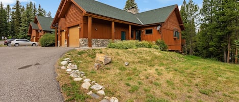 A lodge with a stone foundation, wooden exterior, and a green roof, surrounded by a grassy area and trees.