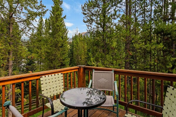 A wooden deck with a round table and two chairs, surrounded by dense forest.