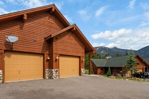A wooden cabin with a garage, stone accents, and a mountain backdrop.