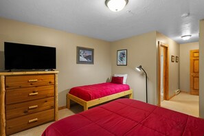 Un dormitorio con un aparador de madera, una cama con una manta roja y un televisor sobre el aparador, además de una puerta que da a otra habitación.