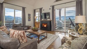 Un salon spacieux doté d’une cheminée, de sièges confortables et de grandes fenêtres offrant une vue sur les montagnes.