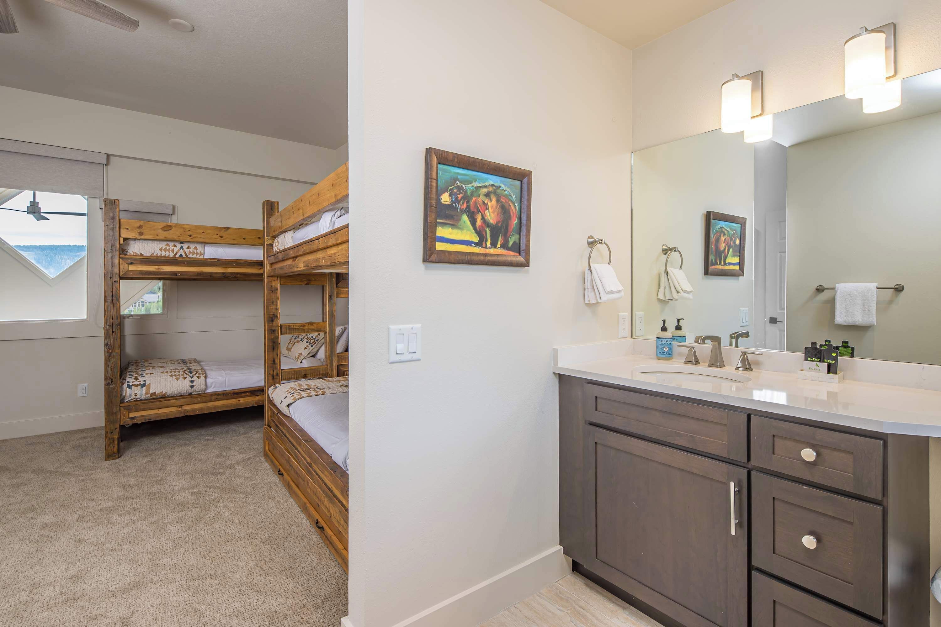 A bunk bed with a skylight, a bathroom with a sink and mirror, and two wall-mounted paintings.