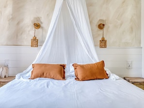 A bed with a canopy, two pillows, a wall-mounted light fixture, and a small decorative item on the nightstand.
