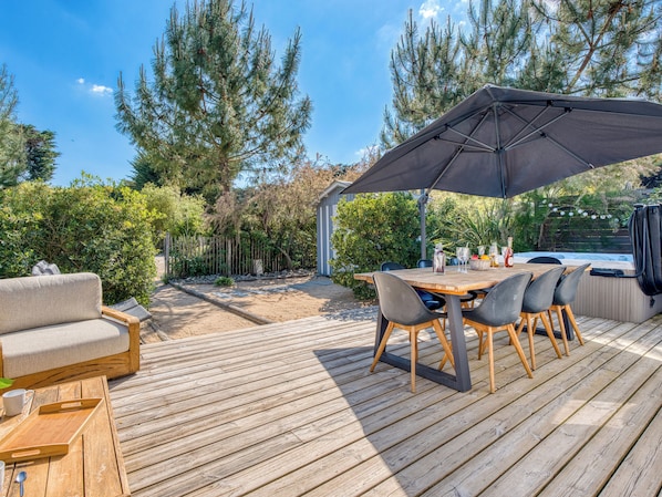 A wooden deck with a table and chairs, a sofa, and a hot tub.