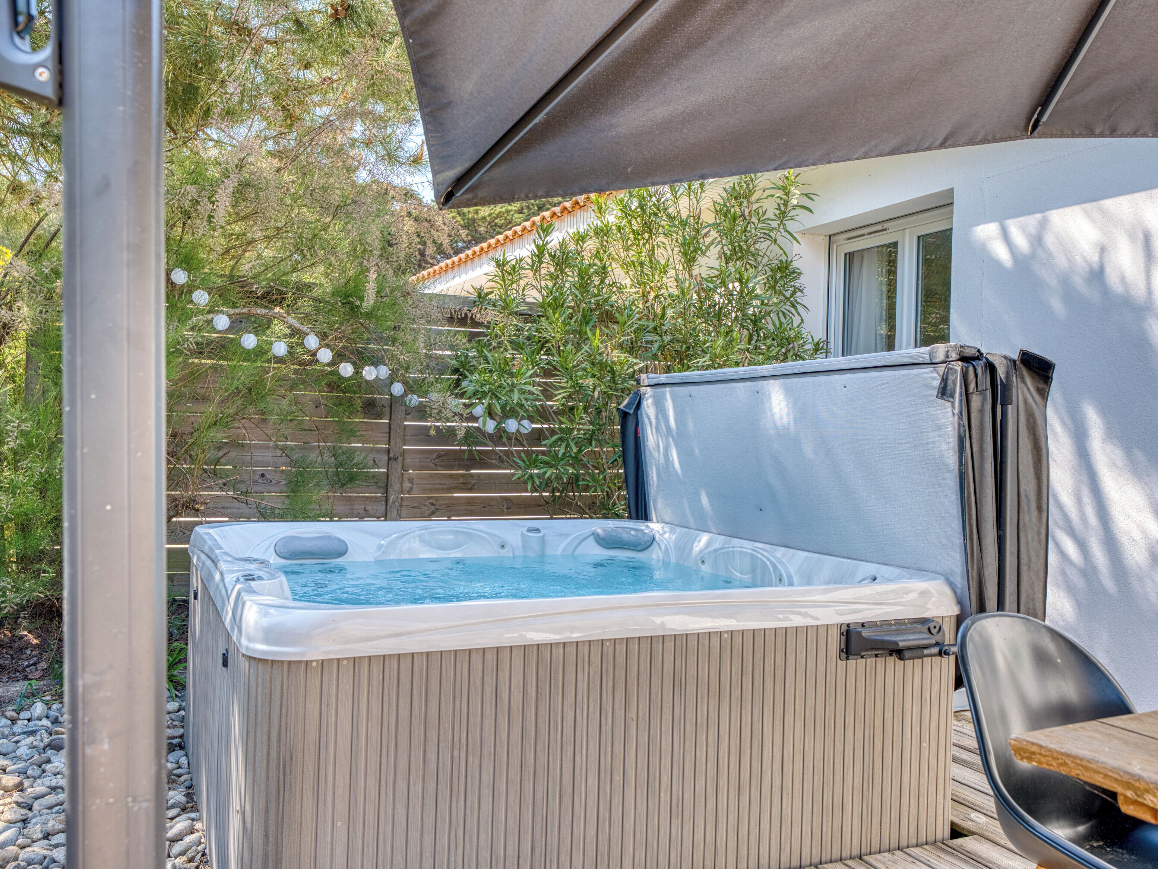Un jacuzzi con una terraza de madera, una sombrilla y una valla de madera al fondo.