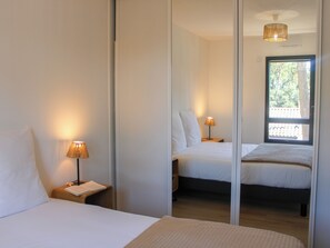 A bedroom with a bed, bedside lamp, and a window with a view of trees. - Villa Pinède: 800m from Beach, Private Jacuzzi, Pine Forest, Sleeps 8 (Bretignolles-sur-Mer)
