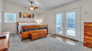 Une chambre à coucher comprenant un lit, une commode en bois, un ventilateur de plafond et une porte-fenêtre coulissante donnant sur l’extérieur.