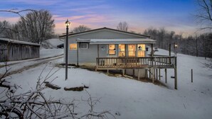 Une maison de plain-pied avec un porche et une terrasse, entourée d’un paysage enneigé et d’arbres.