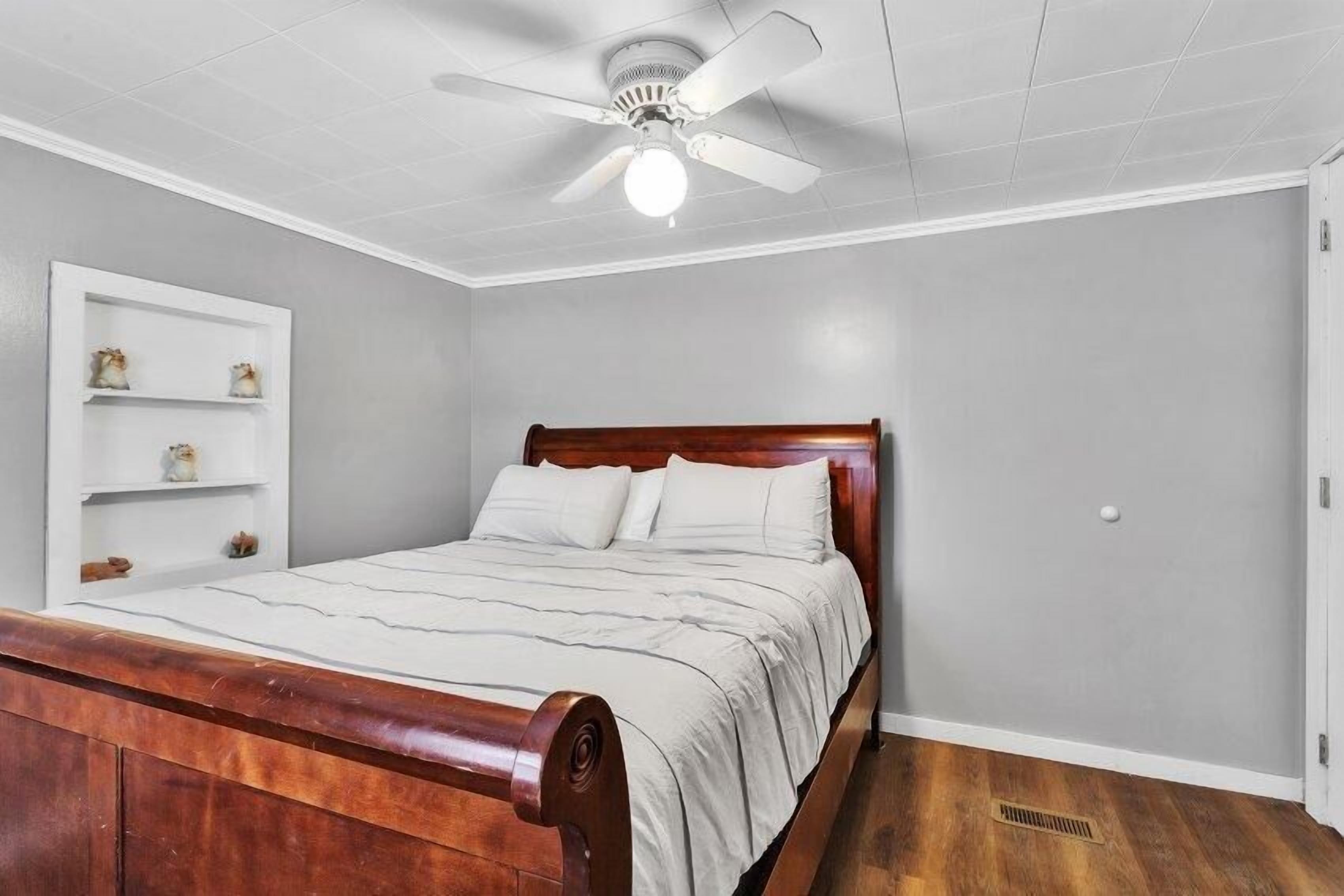 Un dormitorio con una cama de madera, un ventilador de techo y un estante blanco adosado a la pared.
