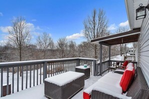 Une terrasse extérieure couverte, aménagée avec des meubles en osier et dotée d’une rambarde, qui offre une vue sur un paysage enneigé.