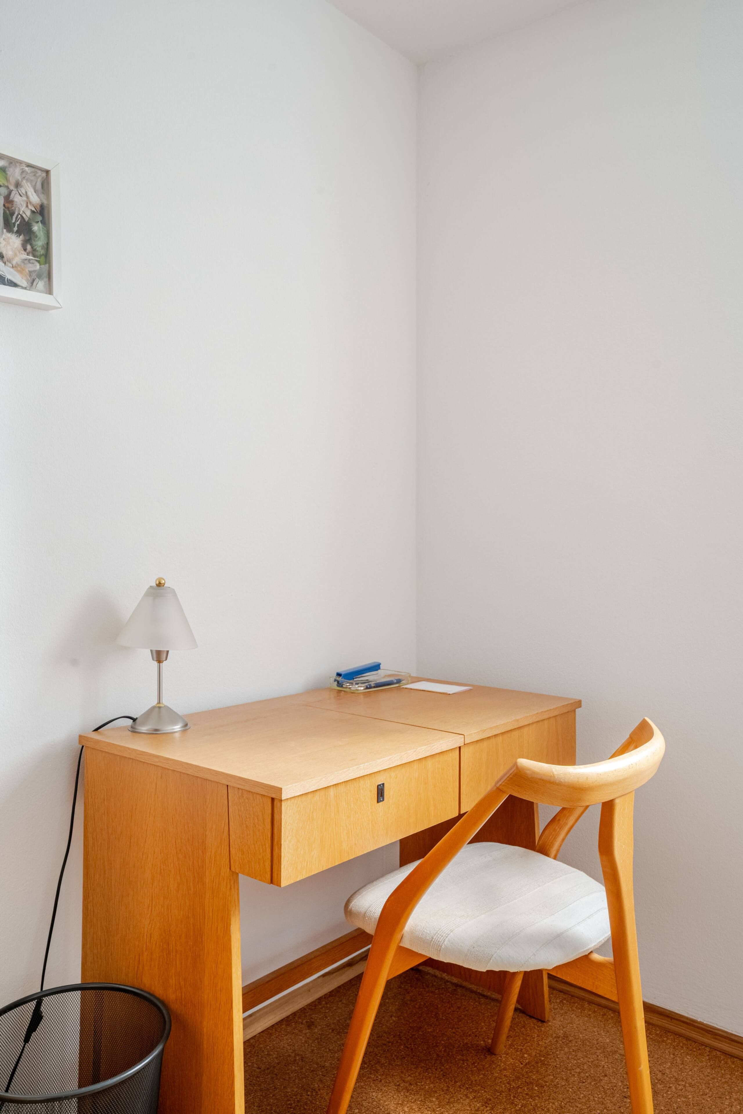 Ein kleiner Schreibtisch mit Stuhl, Lampe und Mülleimer.