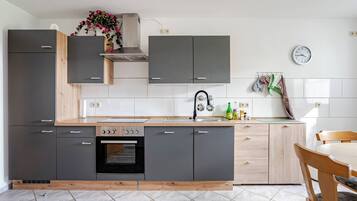 Une cuisine moderne avec des meubles gris, un plan de travail en bois, un four encastré et un évier.
