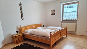 A bedroom with a wooden bed, a bedside table, a nightstand, a window with a view of trees, and a radiator. - Spacious first floor apartment for the whole family near Buchenberg in Allgäu (Buchenberg)
