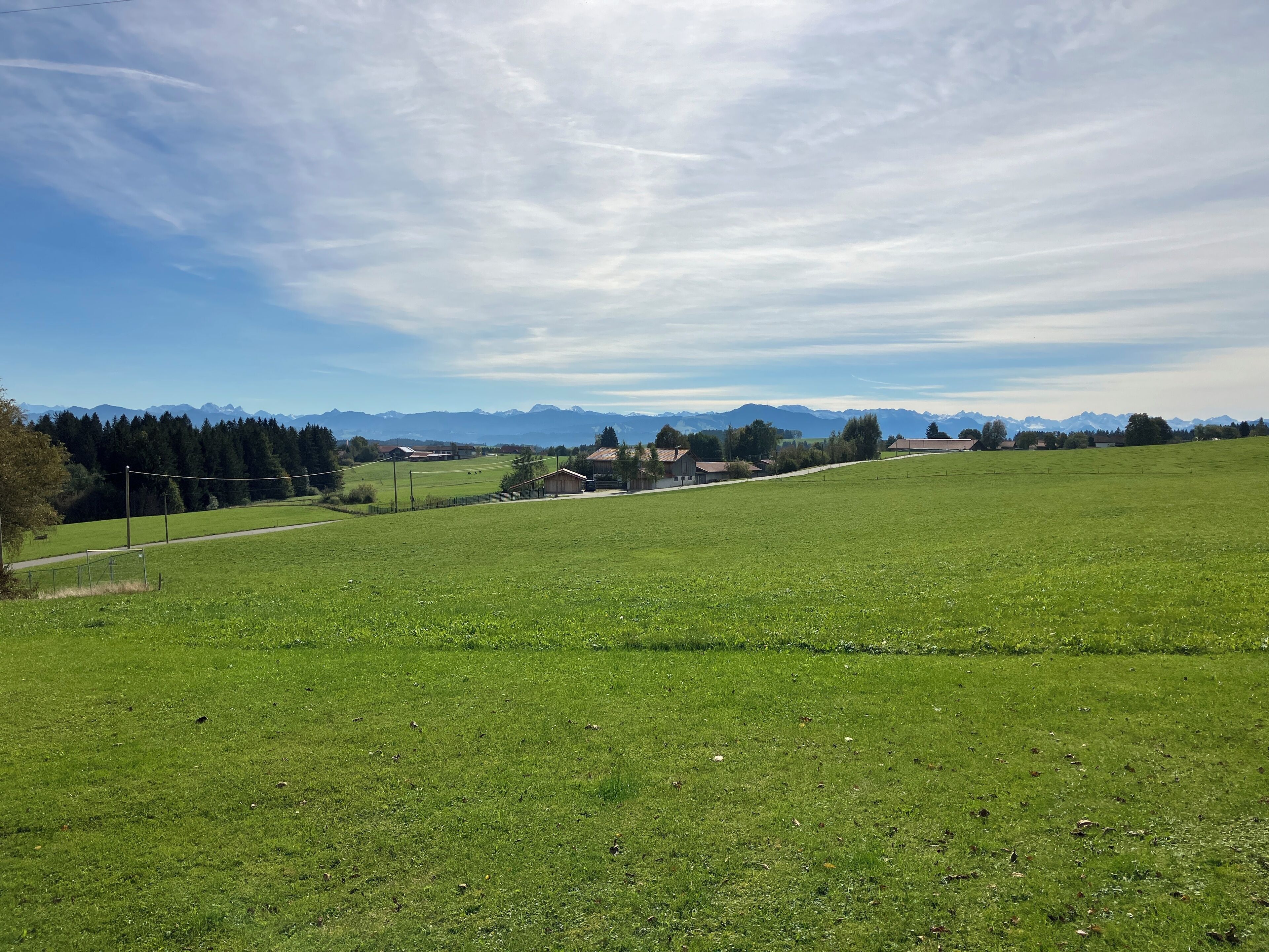 A rural landscape with a green field, a few buildings, and mountains in the background.