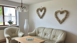 A living room with a beige leather sofa, a wooden coffee table, and two armchairs. There are two heart-shaped wall decorations and a tall white vase. - Spacious first floor apartment for the whole family near Buchenberg in Allgäu (Buchenberg)