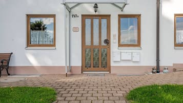 Ein Gebäudeeingang mit einer nummerierten Tür, zwei Fenstern, einer Bank und einem Fußweg.
