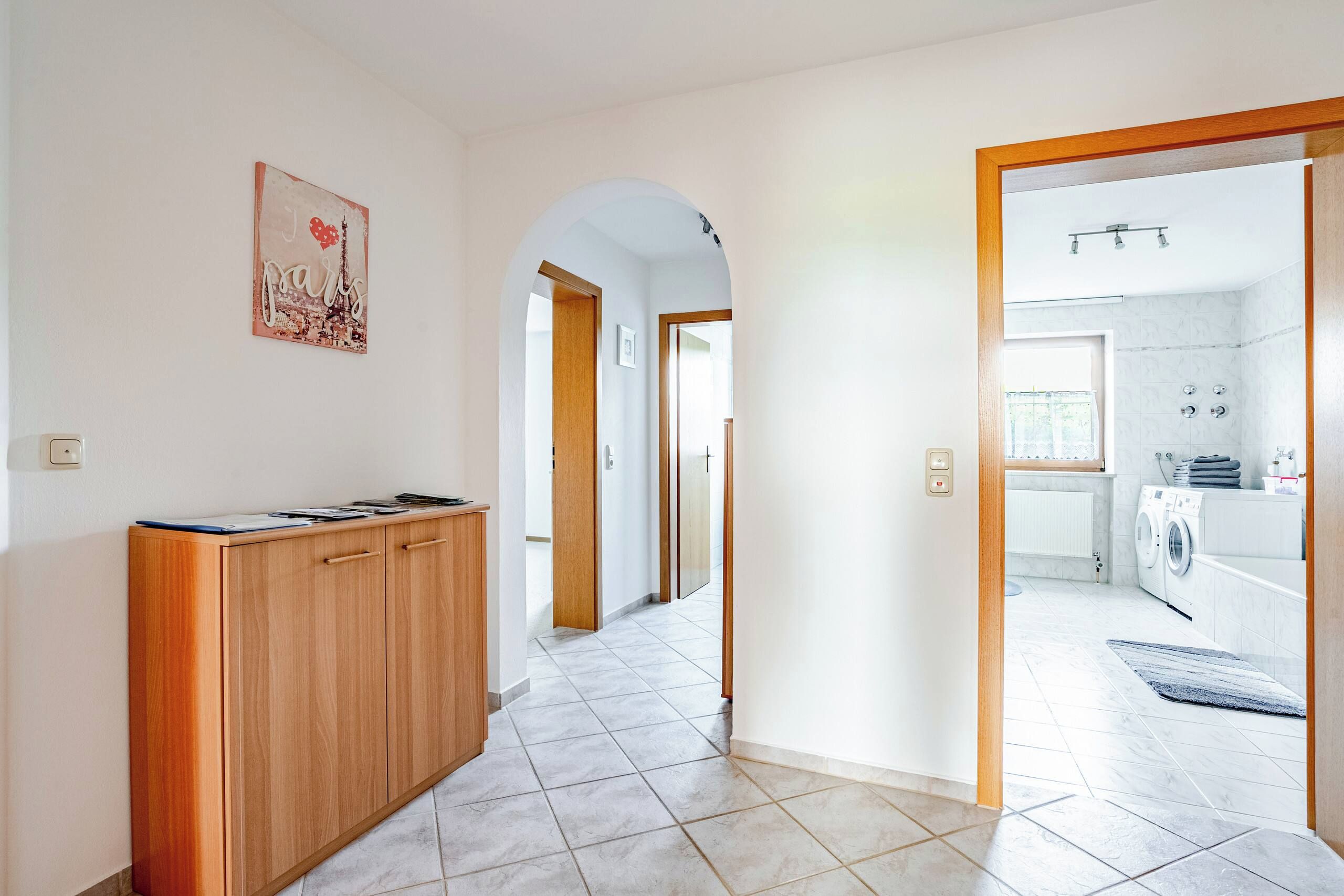 A hallway with a wooden cabinet, a door leading to a laundry area, and a tiled floor.