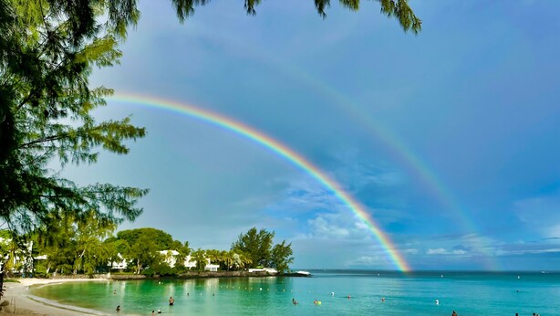 Une plage avec un arc-en-ciel, une eau turquoise cristalline et un rivage sablonneux.