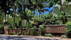 Un panneau indiquant l’entrée de Cape Bay, avec une clôture en bois et une végétation tropicale.