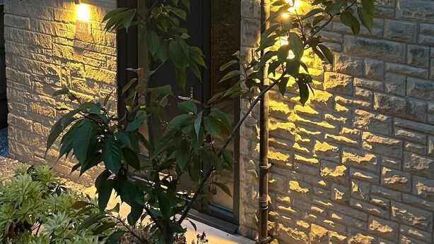 Un bâtiment en pierre avec une fenêtre sombre et une porte, éclairés par des lumières chaleureuses.