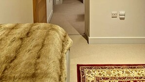Une chambre d’hôtel avec une porte en bois, un miroir au mur, un sol recouvert de moquette et un lit avec un oreiller rouge.