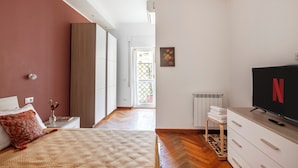 A bedroom with a bed, a TV, a radiator, and a window with a view of the outside.