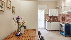 A compact kitchen with white cabinets, a blue stove, and a window with a curtain.