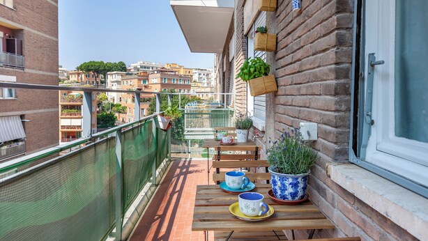 A balcony with a wooden table, chairs, and potted plants.